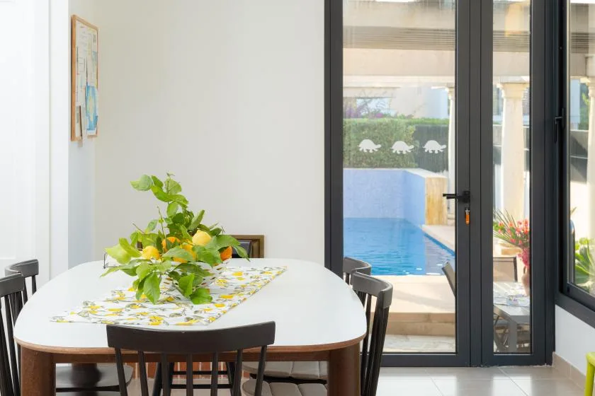 Comedor con una mesa junto a grandes ventanales que dan a una piscina.