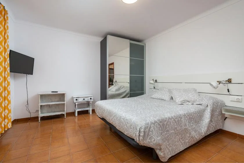Un dormitorio con una cama grande, un armario con espejo y un televisor en la pared.