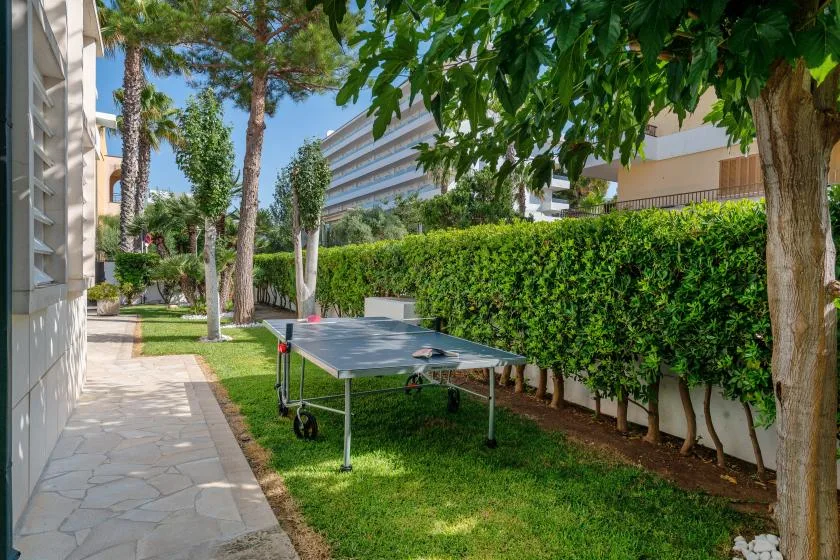 Una mesa de ping-pong está en un patio exterior con césped junto a un seto.