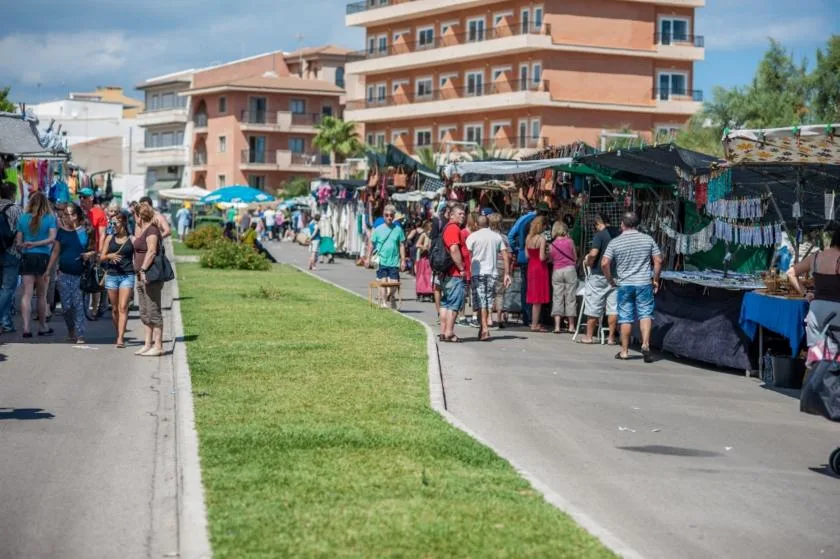 Un mercado al aire libre bordea un paseo pavimentado junto a una franja de césped y edificios de apartamentos.