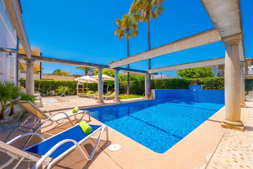 Una piscina junto a un patio soleado con tumbonas y vigas elevadas.