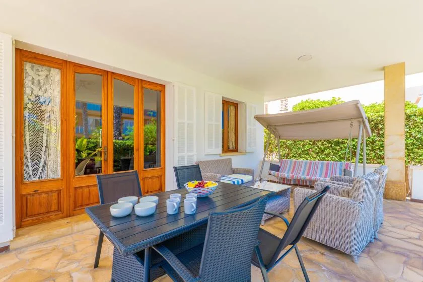 Comedor exterior cubierto con una mesa y asientos junto a unas puertas de vidrio.