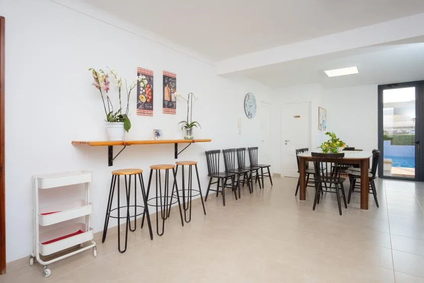 Un comedor luminoso tiene una barra larga con taburetes y una mesa con sillas.