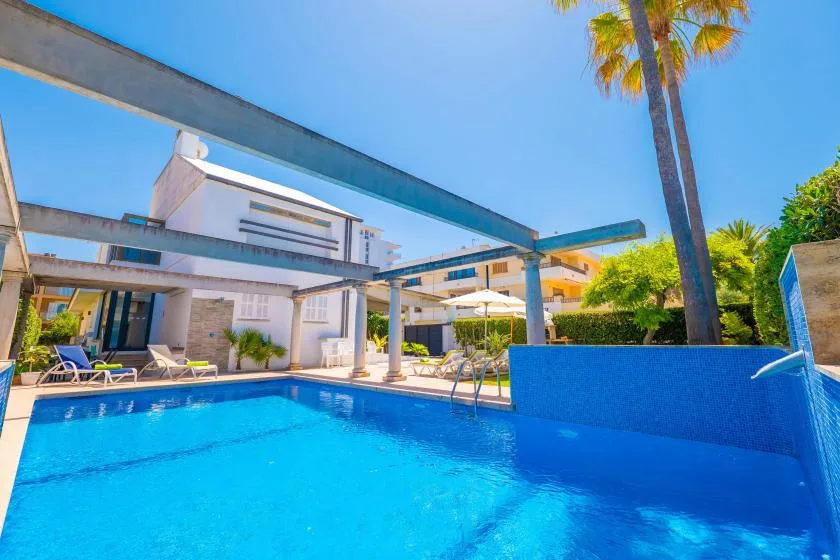 Una piscina al aire libre junto a un edificio blanco moderno y palmeras.