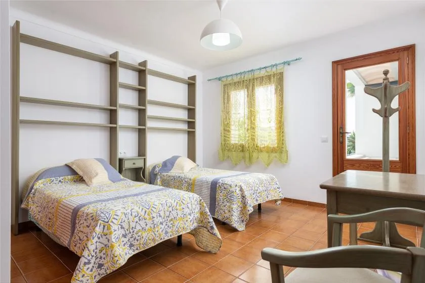 Un dormitorio con dos camas individuales, estanterías empotradas y una ventana.