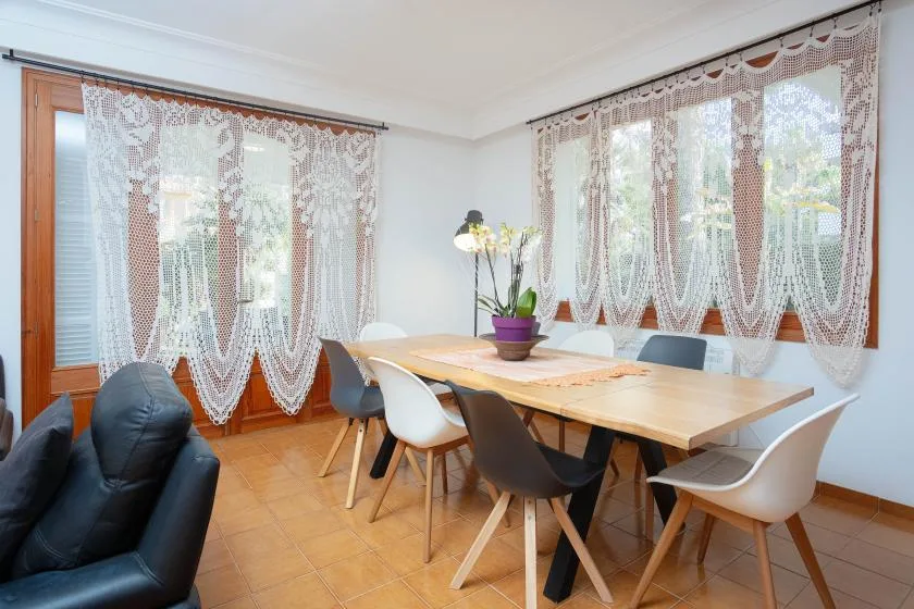 Un comedor con una mesa larga de madera, asientos y cortinas de encaje.