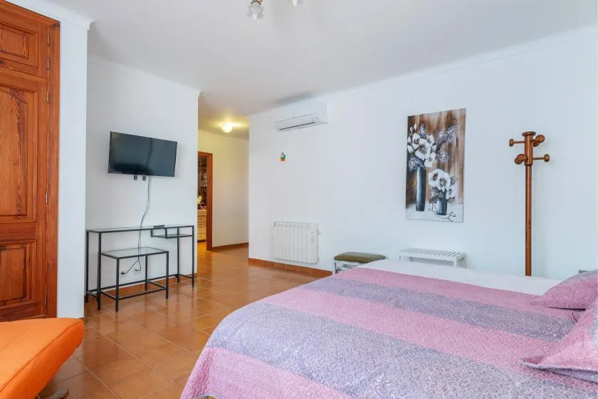Un dormitorio con una cama, un televisor en la pared y un armario de madera.