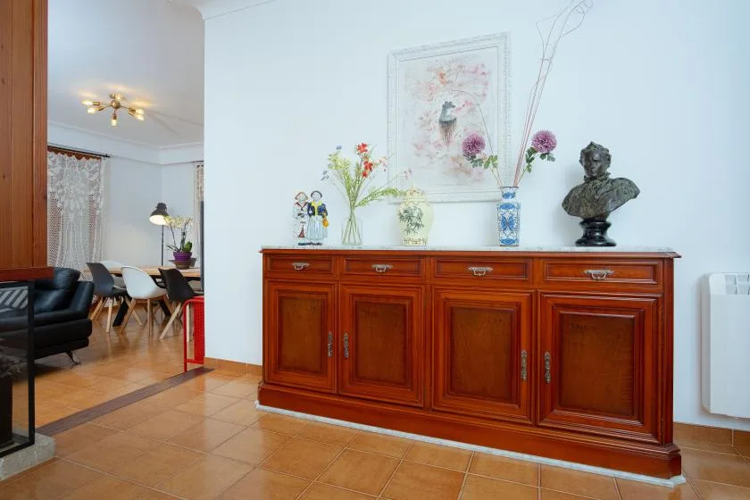 Una sala amueblada con un mueble de madera, flores y una obra enmarcada.
