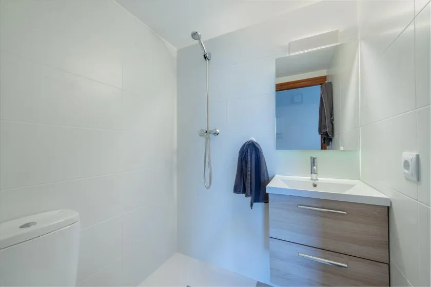 Un baño luminoso con ducha, inodoro y lavabo con mueble.