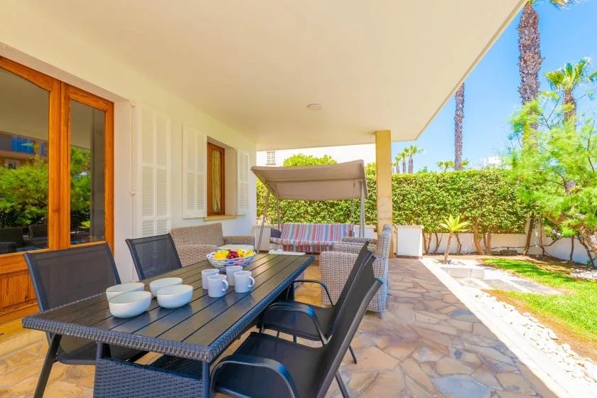 Un patio cubierto tiene una mesa de comedor y asientos junto a un jardín.