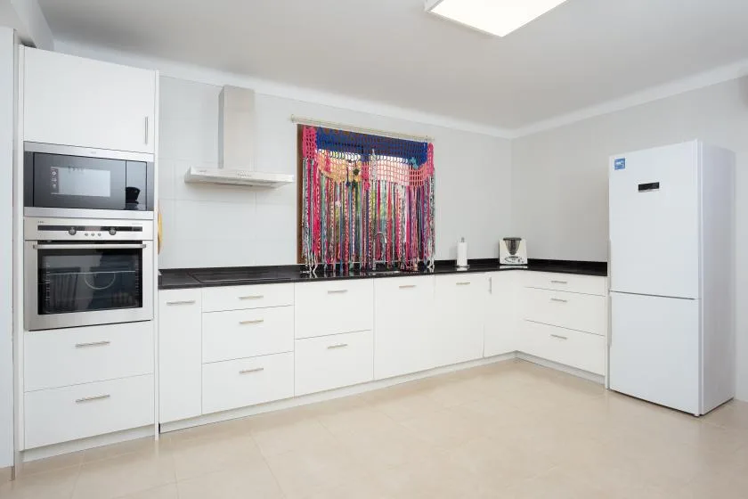 Una cocina luminosa con gabinetes blancos, encimeras negras y una cortina colorida en la ventana.