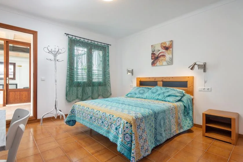 Un dormitorio con una cama cubierta con ropa de cama azul estampada y una ventana con cortinas.