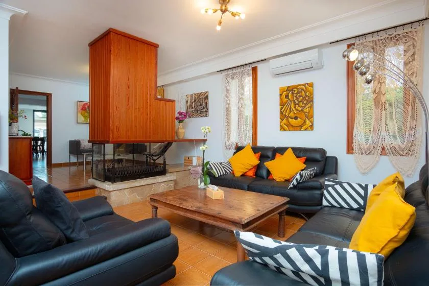 Una sala de estar con asientos oscuros, una mesa de centro de madera y una chimenea central.