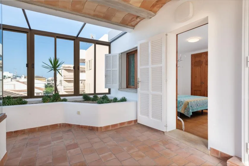 Un solárium luminoso con grandes ventanas y una puerta abierta a un dormitorio.