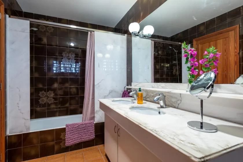 Un baño con azulejos, un tocador largo, lavabo y espejo.