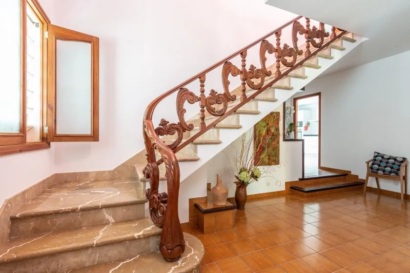 Una escalera de baldosas con una barandilla ornamentada sube junto a una ventana luminosa.