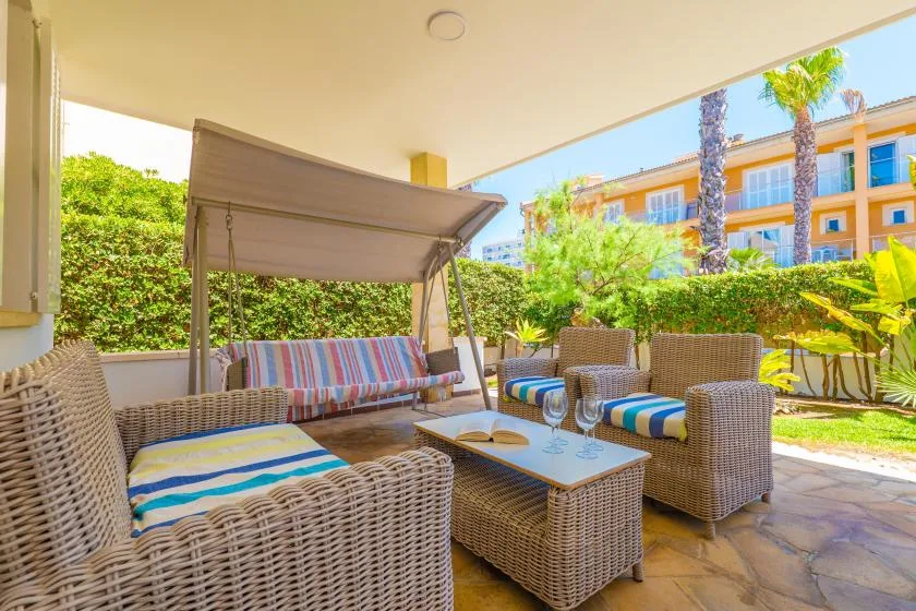 Una zona de estar en un patio sombreado, con muebles tejidos y un columpio a rayas.