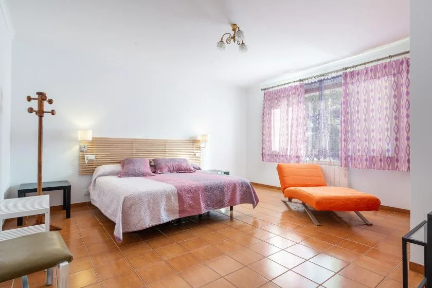 Un dormitorio con una cama, cortinas estampadas y una butaca naranja.