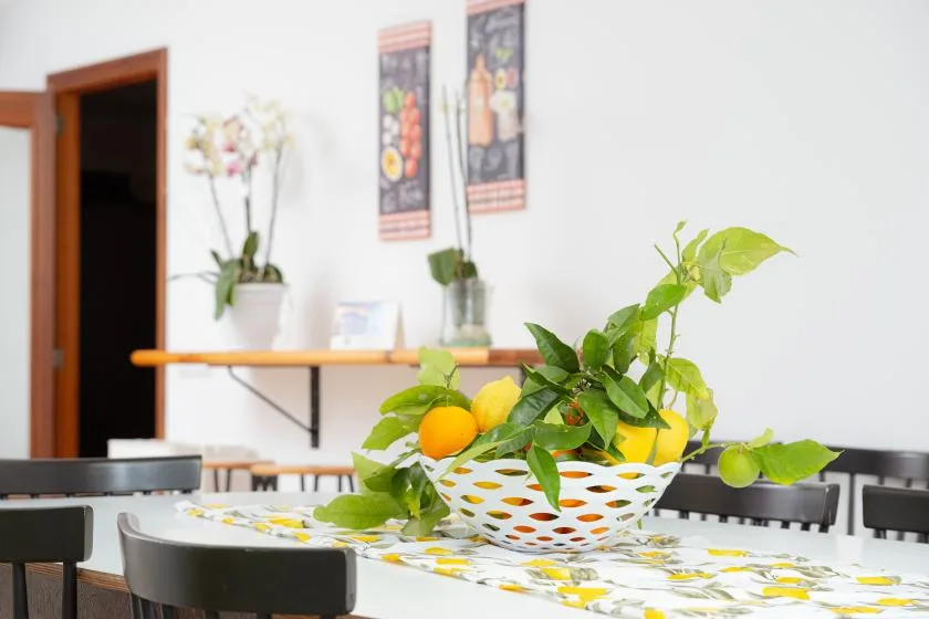 Un comedor con un frutero y plantas de hojas verdes sobre la mesa.