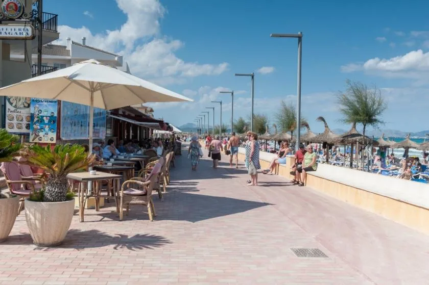 Un concurrido paseo junto al mar con mesas de café al aire libre y sombrillas.