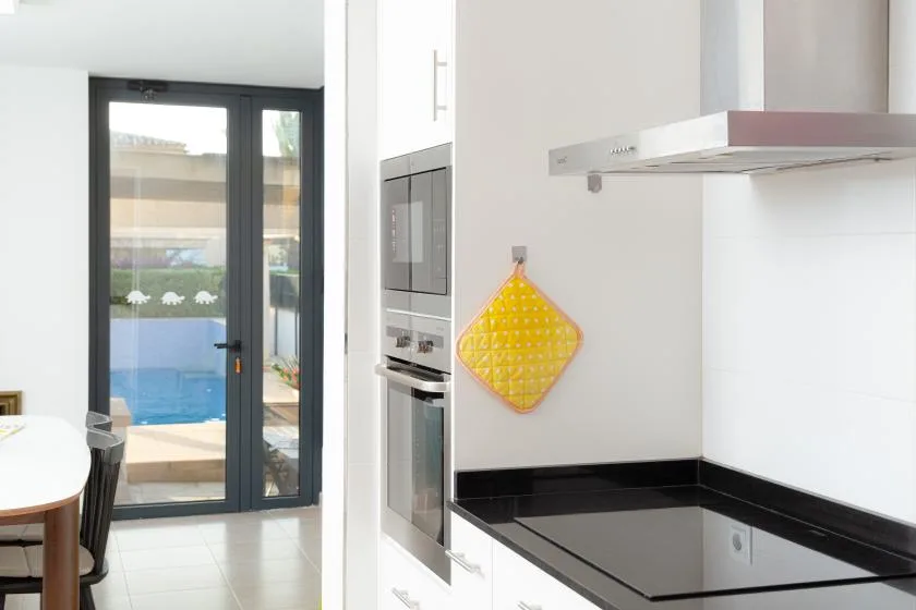 Una cocina moderna con una placa negra y un horno empotrado junto a puertas de vidrio.