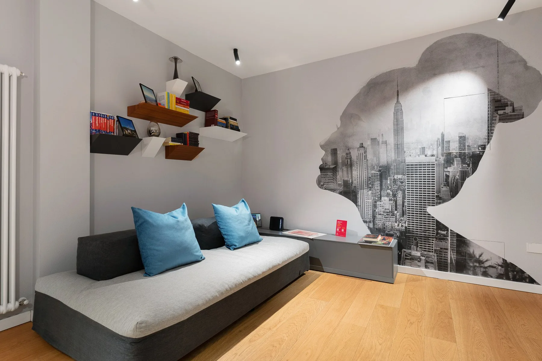 Un dormitorio con una cama baja, estantes de pared y un gran mural urbano.
