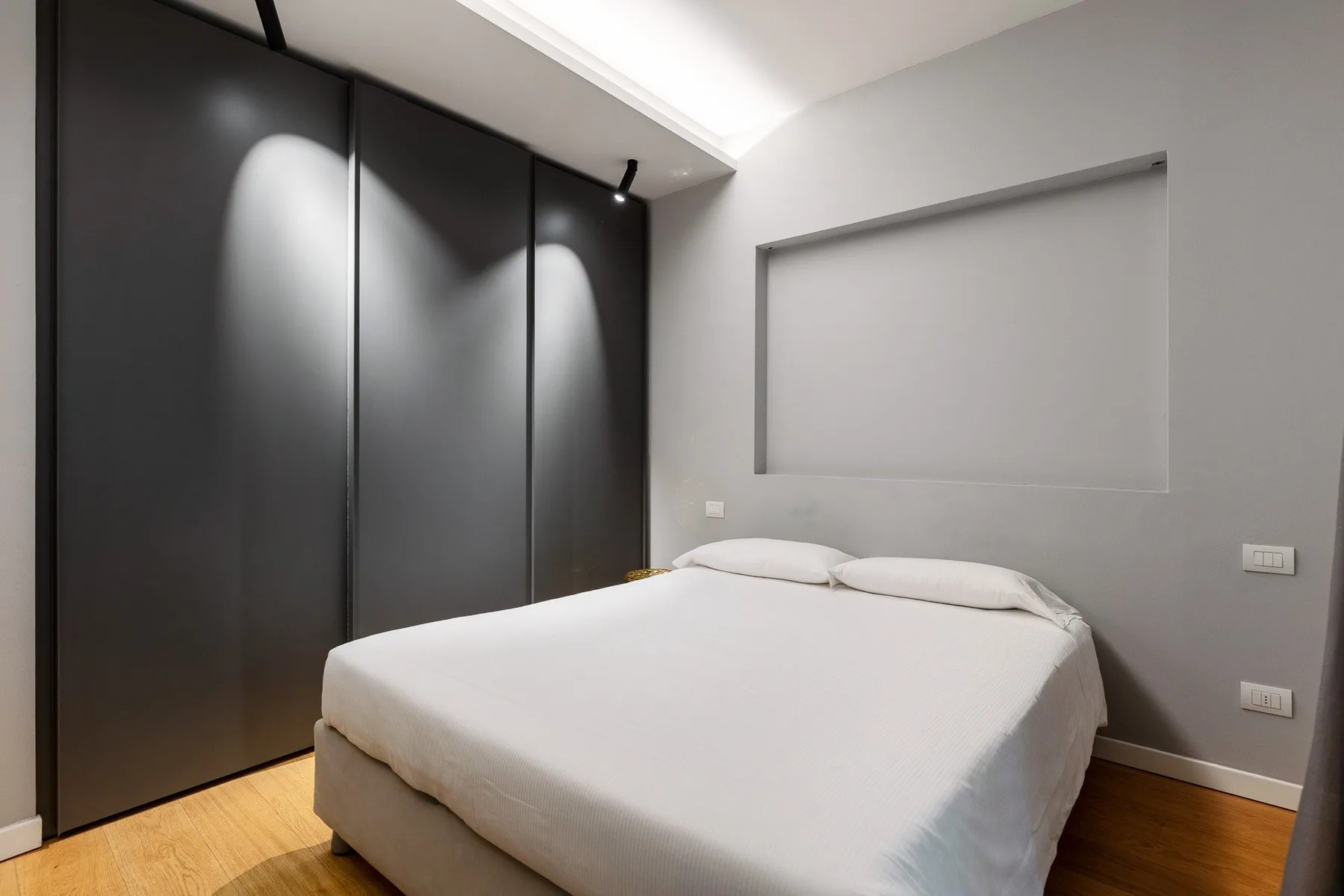 A bedroom with a neatly made bed and dark built-in wardrobes.