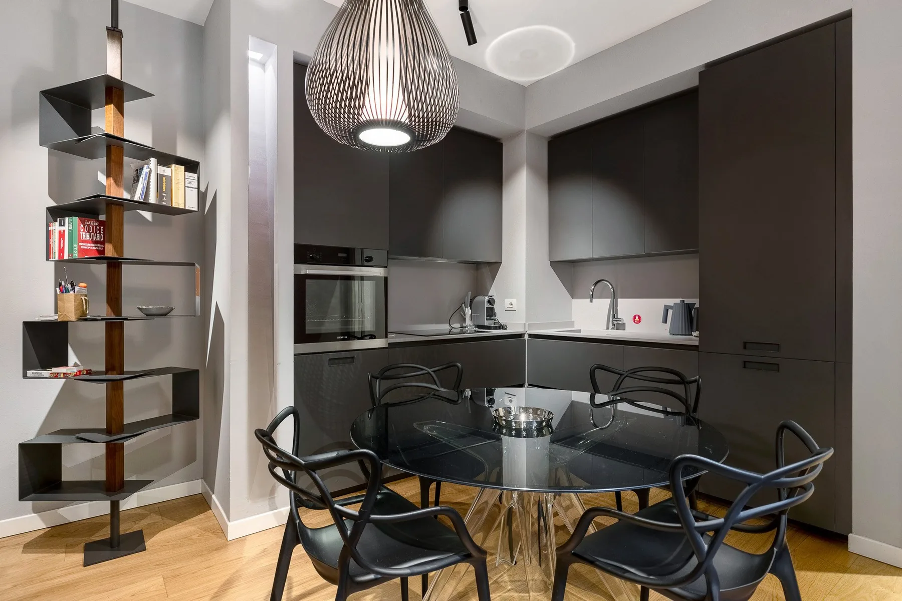 A modern kitchen and dining area with dark cabinetry and a round glass table.
