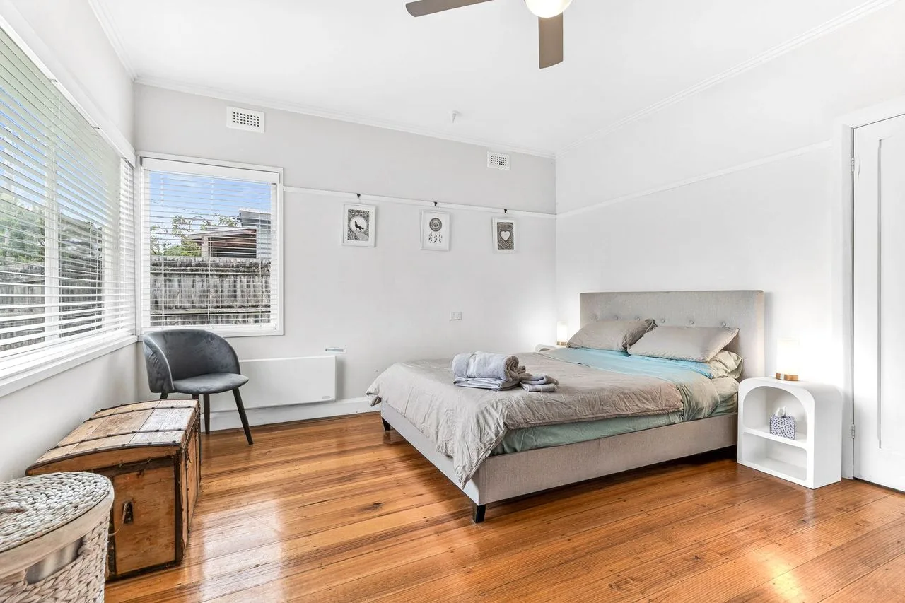 A bright bedroom with a bed, wooden flooring, and wide windows.