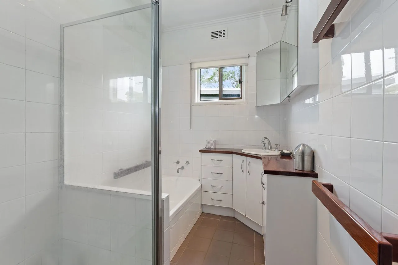 A bright tiled bathroom with a bathtub, sink, and small window.