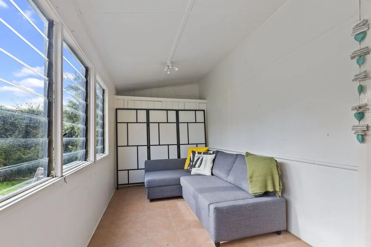 A bright enclosed sitting area with a gray sectional and large windows.