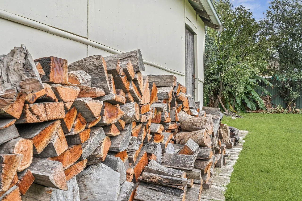 A large stack of cut firewood beside a house and lawn.
