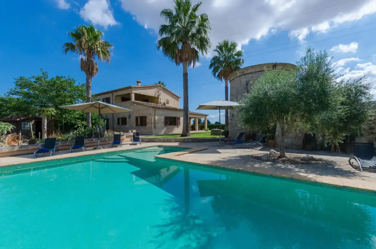 Una piscina al aire libre junto a una casa y palmeras.