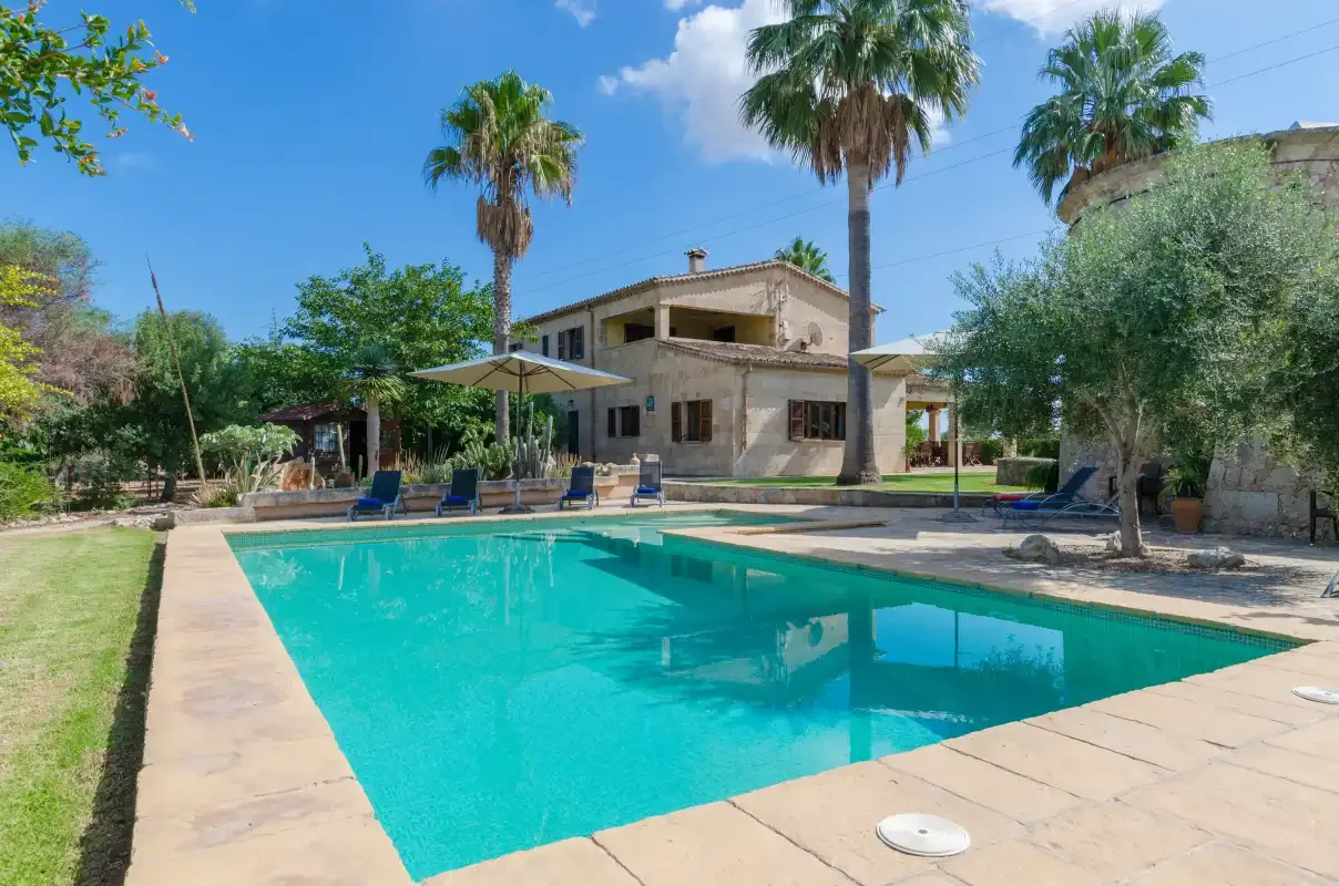 Una piscina ocupa el primer plano frente a una casa y un jardín.