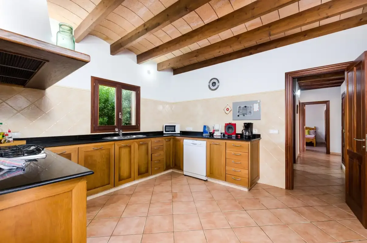 Una cocina amplia con muebles de madera, suelo de baldosas y vigas vistas en el techo.