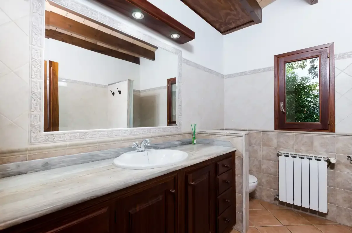 Un baño con un mueble de lavabo largo, un espejo grande y una ventana.