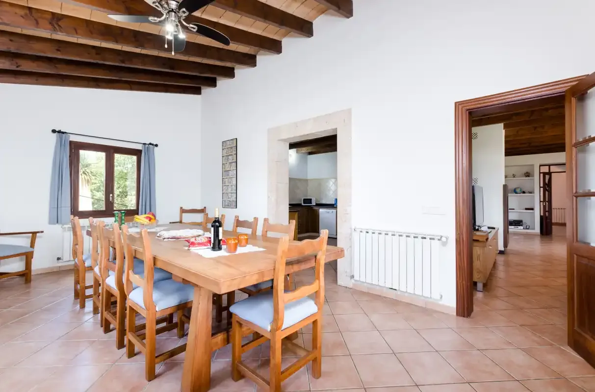 Comedor con una mesa y sillas de madera bajo vigas de techo a la vista.
