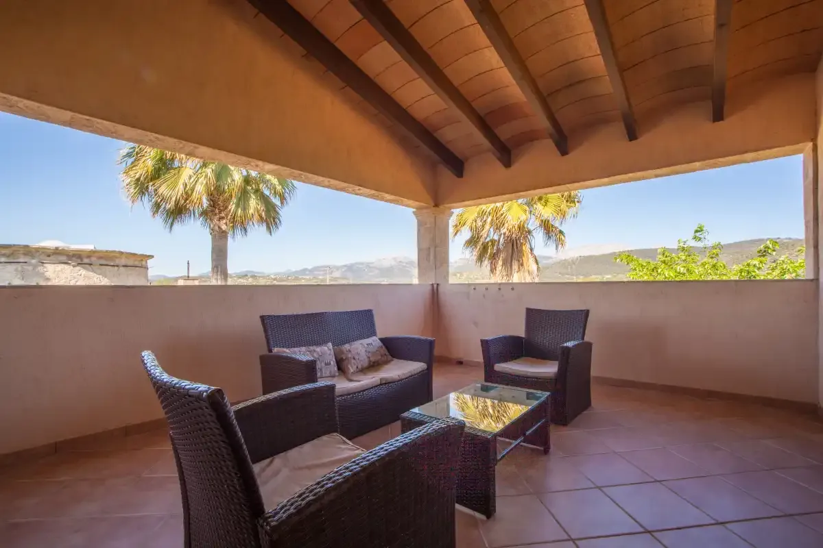 Un patio cubierto con asientos de mimbre y vistas de palmeras y colinas.