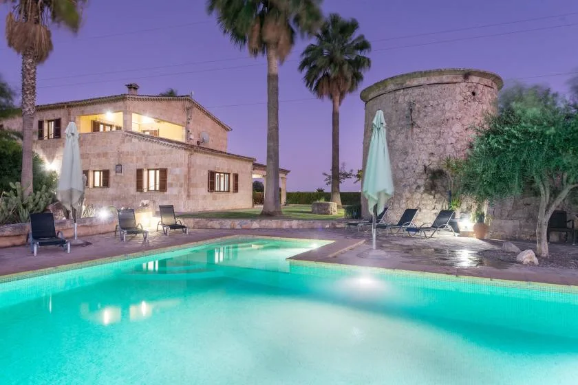 Una piscina al aire libre junto a un edificio de piedra, con asientos y palmeras.