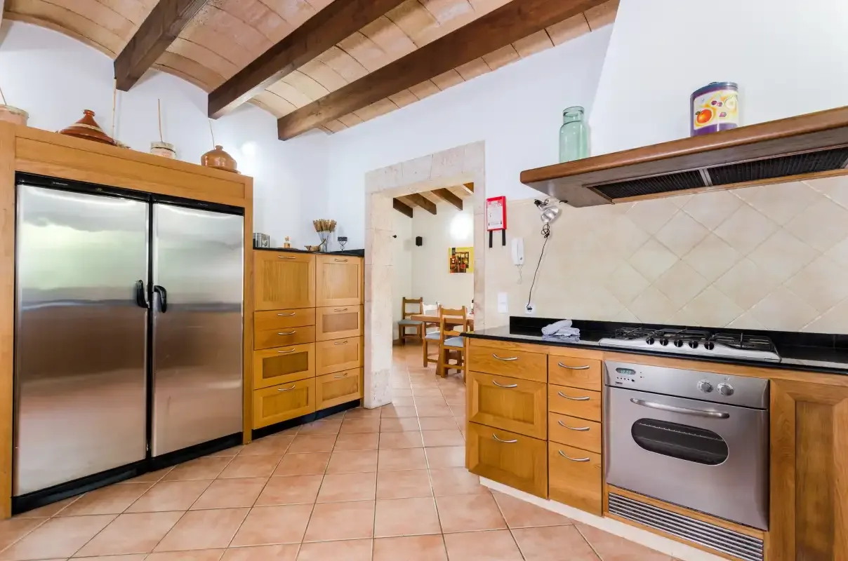 Una cocina con armarios de madera, electrodomésticos de acero inoxidable y suelo de baldosas.