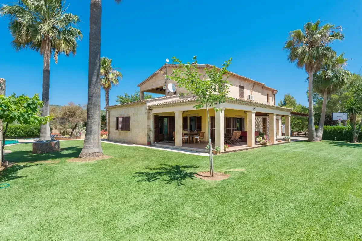 Una casa de dos plantas está junto a un césped verde y palmeras.