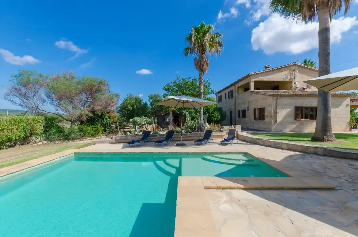 Una piscina junto a una casa, con asientos y palmeras.
