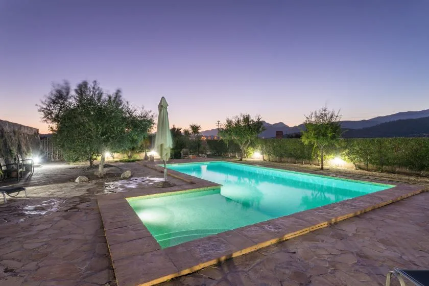 Una piscina al aire libre junto a un patio de piedra al anochecer.
