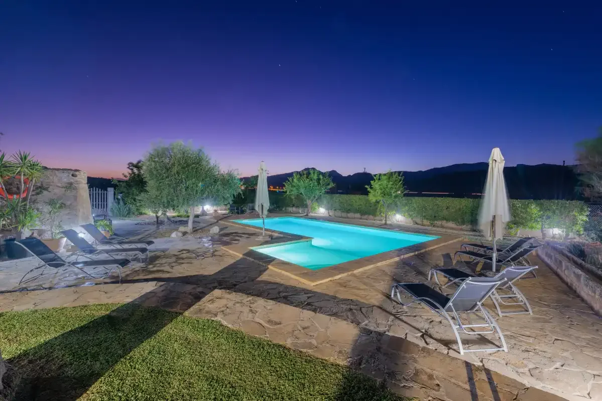 Una piscina exterior iluminada junto a asientos de descanso al anochecer.