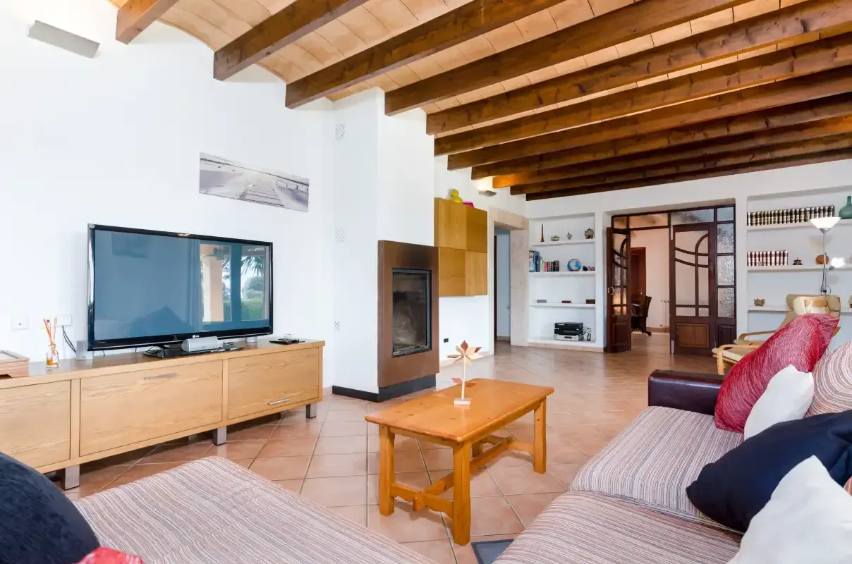 Una sala de estar con asientos, un televisor y vigas de madera a la vista en el techo.
