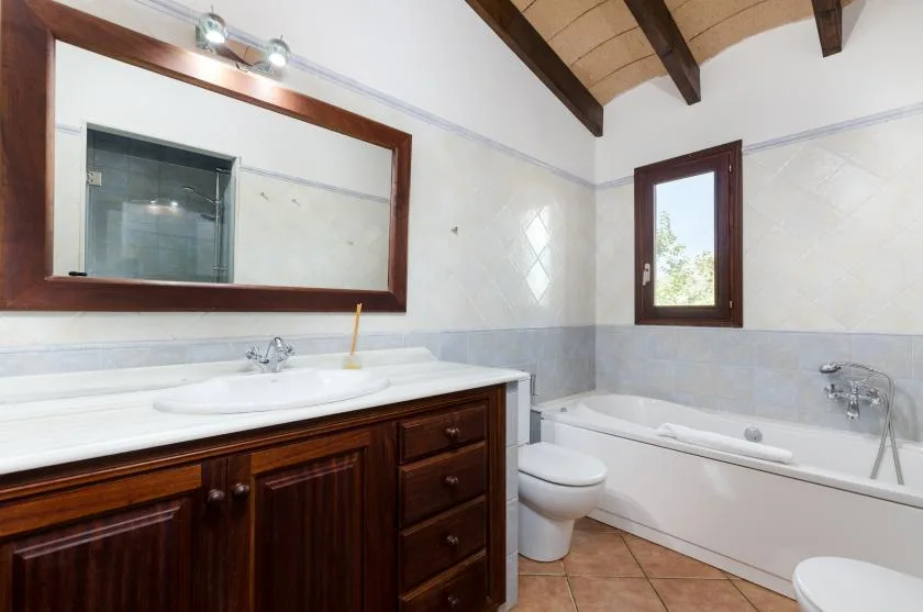 Un baño con lavabo, espejo y bañera bajo un techo inclinado.