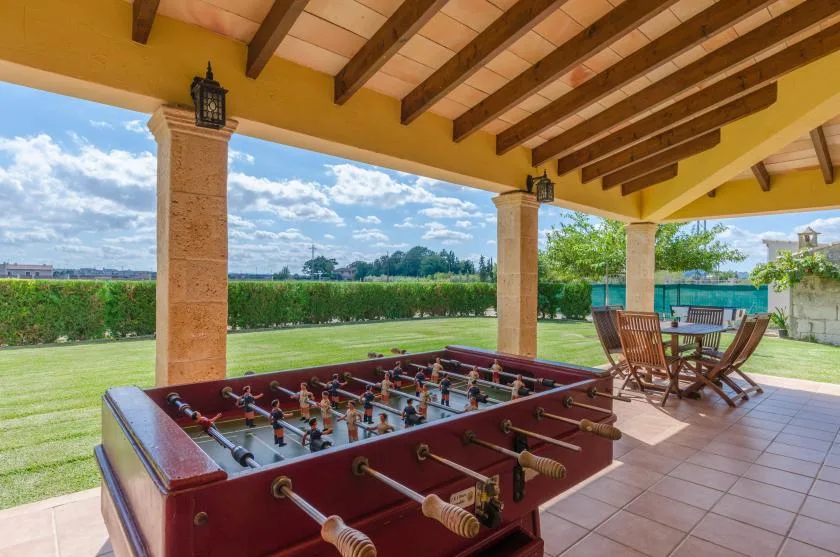 Un patio cubierto tiene una mesa de futbolín junto al césped y asientos de comedor.