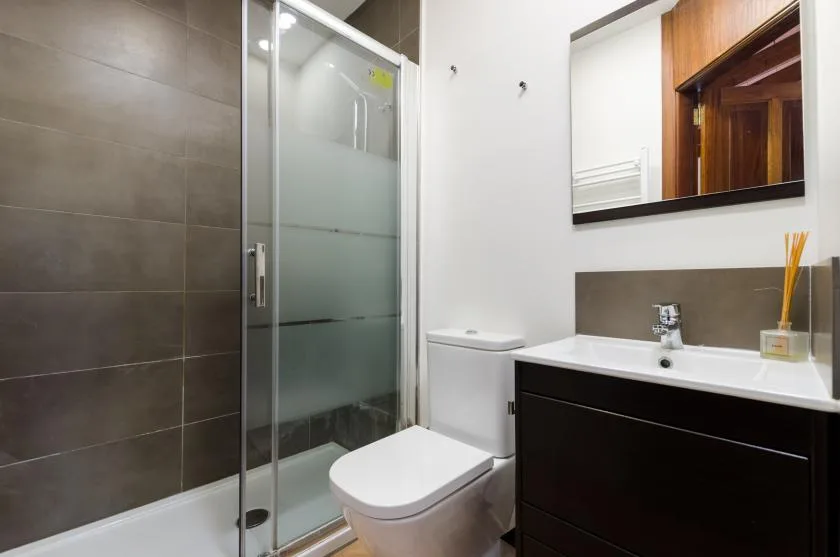 Un baño con ducha de vidrio, inodoro y mueble oscuro.