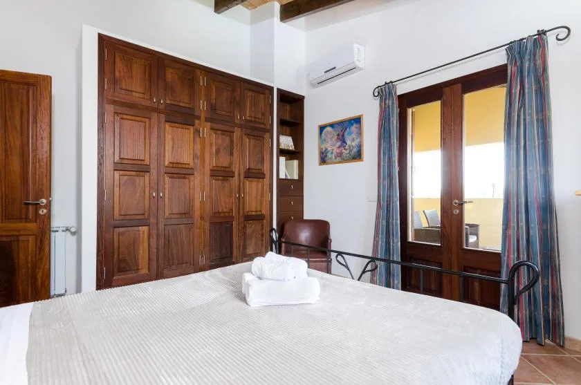 Un dormitorio con cama, armario de madera y una puerta acristalada con cortinas.