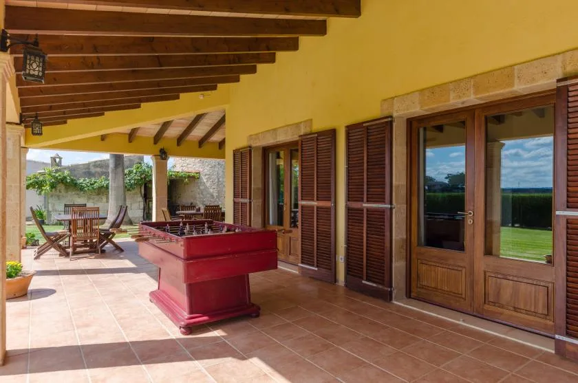 Un patio cubierto con una mesa roja, puertas de madera y asientos al aire libre.
